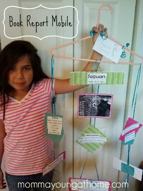 A girl stands next to a book report mobile done from a wire hanger additionally index cards as an sample of creative book message ideas